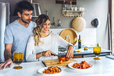Junge Frau hackt Tomaten, während sie ein Abendessen kocht und ein Mann zusieht - EHF00942