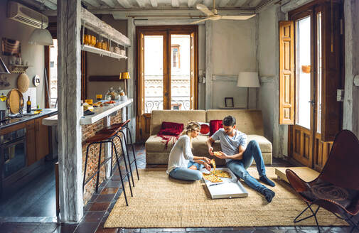 Junges Paar sitzt auf dem Boden des Wohnzimmers und isst Pizza aus einem Karton - EHF00948