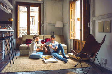 Young couple sitting on floor of living room and eating pizza from box - EHF00949