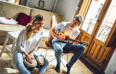 Glückliches junges Paar spielt Duett mit Schlagzeug und Gitarre im Wohnzimmer zu Hause - EHF00960