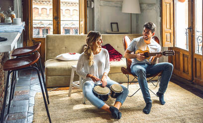 Glückliches junges Paar spielt Duett mit Schlagzeug und Gitarre im Wohnzimmer zu Hause - EHF00961
