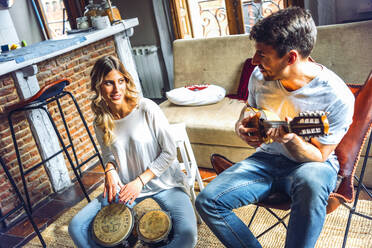 Junges Paar spielt ein Duett mit Schlagzeug und Gitarre im heimischen Wohnzimmer - EHF00962