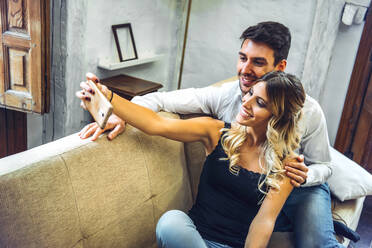 Smiling young couple taking selfie on couch in living room at home - EHF00977