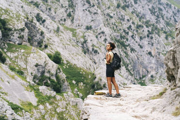 Frau mit Rucksack bewundert die Aussicht, während sie auf einem Bergpfad an der Ruta Del Cares steht, Asturien, Spanien - DGOF01387