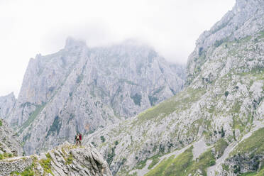 Junger Mann und Frau bewundern die Aussicht, während sie auf einem Berg an der Ruta Del Cares stehen, Asturien, Spanien - DGOF01391