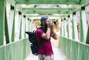 Mann, der auf einer Brücke an der Ruta Del Cares, Asturien, Spanien, durch eine Kamera fotografiert - DGOF01406