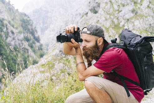 Junger Mann, der auf einem Berg an der Ruta Del Cares, Asturien, Spanien, durch eine Kamera fotografiert - DGOF01410