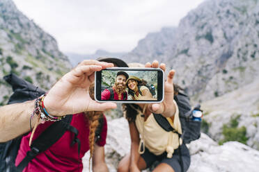 Paar, das ein Selfie mit dem Handy macht, während es auf einem Felsen an der Ruta Del Cares sitzt, Asturien, Spanien - DGOF01420
