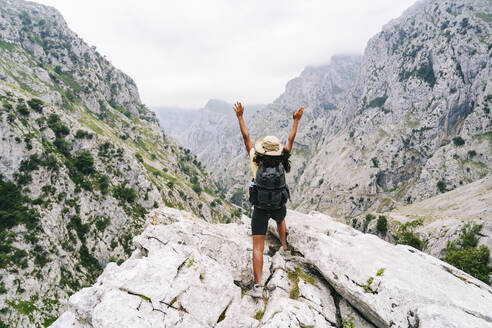 Sorglose Frau mit erhobener Hand auf einem Berggipfel an der Ruta Del Cares, Asturien, Spanien - DGOF01422