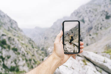 Man's hand holding phone while taking photo of carefree woman at at Ruta Del Cares, Asturias, Spain - DGOF01424