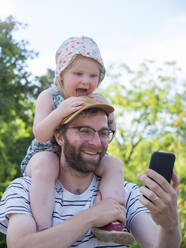 Tochter streckt die Zunge heraus, während der Vater ein Selfie mit dem Smartphone macht - LAF02472