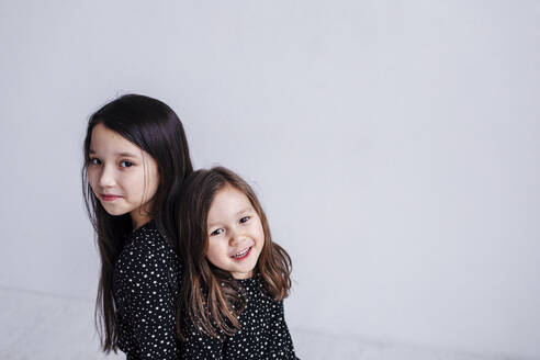 Cute sisters standing back to back against white background in studio - OGF00510