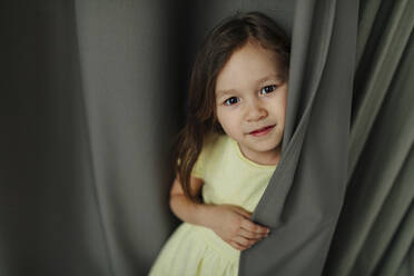 Girl standing against curtain at home - OGF00514