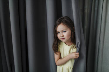 Cute girl standing against gray curtain at home - OGF00515