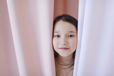 Girl hiding behind curtain at home stock photo