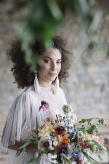 Young woman in wedding dress holding bouquet while standing against wall - ALBF01496