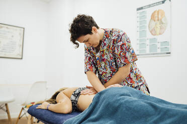 Osteopathische Therapeutin bei der Rückenmassage einer Sportlerin im Behandlungsraum - SASF00054