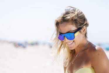 Happy young woman looking down while standing against beach - JCMF01305