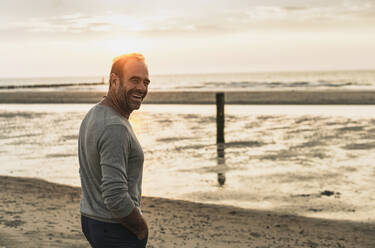 Cheerful mature man standing against sea during sunset at weekend - UUF21196