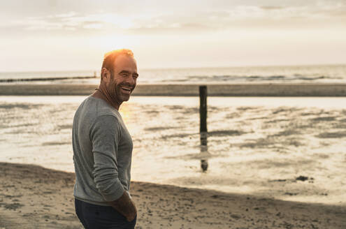 Fröhlicher reifer Mann, der bei Sonnenuntergang am Wochenende am Meer steht - UUF21196