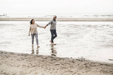 Paar hält Hände beim Spaziergang am Strand gegen den Himmel - UUF21205