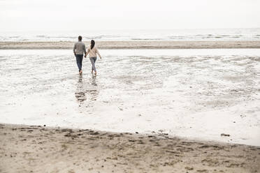 Couple holding hands while walking at beach during sunset - UUF21208