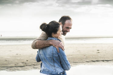 Fröhliches reifes Paar steht am Strand gegen den Himmel am Wochenende - UUF21211