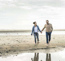 Glückliches Paar hält sich an den Händen und genießt den Sonnenuntergang am Strand - UUF21213
