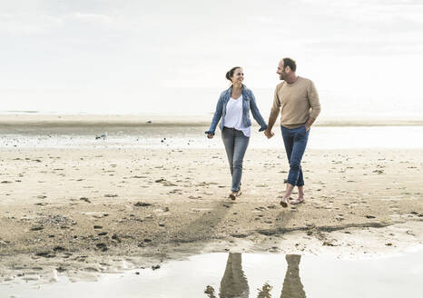 Happy couple holding hands while enjoying weekend at beach during sunset - UUF21214