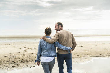 Couple with arms around spending leisure time at beach during weekend - UUF21221