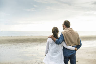 Couple with arms around looking at sea against cloudy sky during sunset - UUF21228