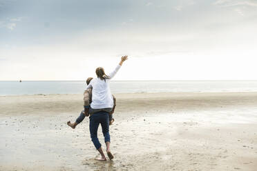 Mature man piggybacking cheerful woman while walking at beach during sunset - UUF21236