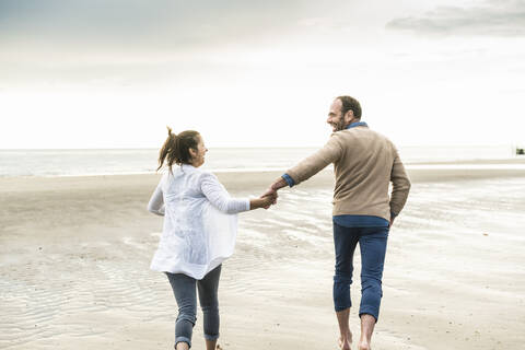 Carefree couple holding hands while running at beach during sunset stock photo