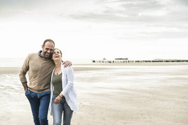 Cheerful couple laughing while walking against sea during sunset - UUF21241