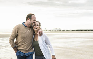 Cheerful man embracing woman while standing against sea during sunset - UUF21242