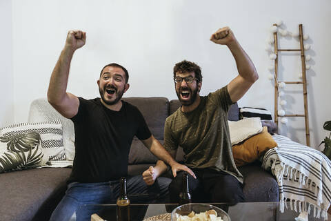 Fröhliche männliche Zuschauer schreien beim Sport im Wohnzimmer, lizenzfreies Stockfoto