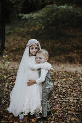 Sister embracing brother at halloween party while standing in forest - GMLF00542