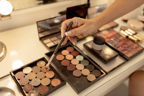 Close-up of beautician's hand with make-up brush and palettes on dressing table - GMLF00554