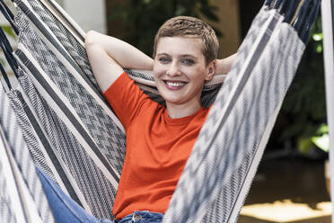 Close-up of smiling beautiful woman with hands behind head swinging in porch - UUF21287