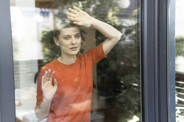 Nachdenkliche Frau, die zu Hause am Fenster steht, gesehen durch Glas - UUF21302