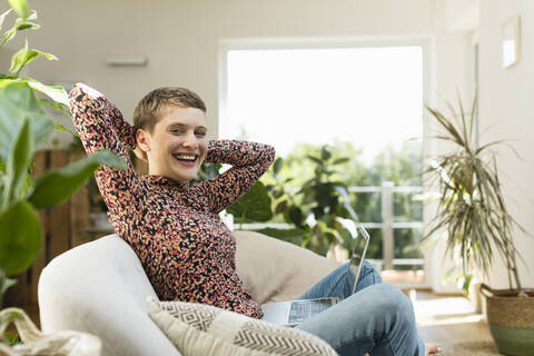 Cheerful woman with hands behind head relaxing on sofa at home stock photo