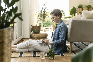 Mid adult woman with short hair using laptop while sitting on carpet at home - UUF21350