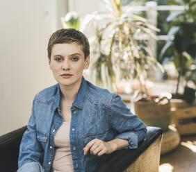 Confident mid adult woman with short hair sitting on chair at home - UUF21356