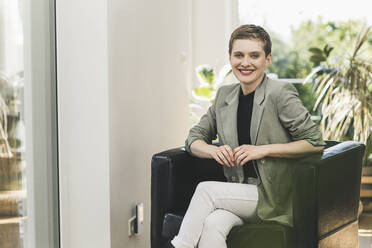 Smiling businesswoman with short hair sitting on armchair at home - UUF21359