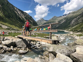 Father with daughters walking on footbridge over river against mountains, Klein Tibet, Tyrol, Austria - GAF00142