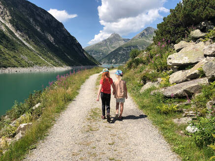 Schwestern gehen am Fluss entlang auf einem Fußweg in Richtung Berge, Klein Tibet, Tirol, Österreich - GAF00143