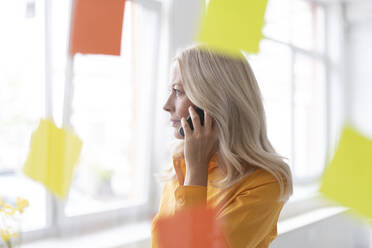 Businesswoman talking over smart phone in home office seen through window - MOEF03196