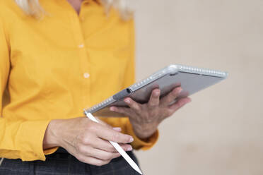 Close-up of female entrepreneur using digital tablet against wall in office - MOEF03207