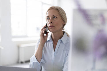 Selbstbewusste Geschäftsfrau, die in ihrem Büro zu Hause sitzt und über ihr Mobiltelefon spricht - MOEF03211