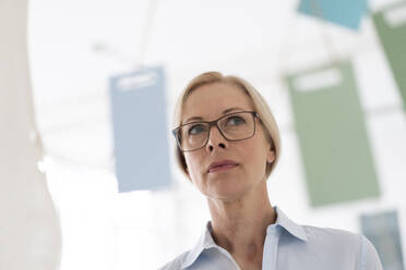 Nahaufnahme einer nachdenklichen Geschäftsfrau mit Brille, die im Büro zu Hause wegschaut - MOEF03217